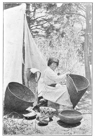 A BASKET MAKER. She is weaving a burden basket. The one to the left is for cooking, and a baby basket stands against the tent